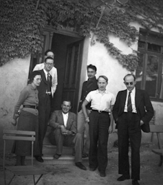 A black and white photo of one woman and six men standing in front of a doorway.