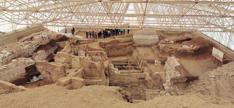 dwelling walls visible at a dusty archaeological dig under a warehouse-type roof