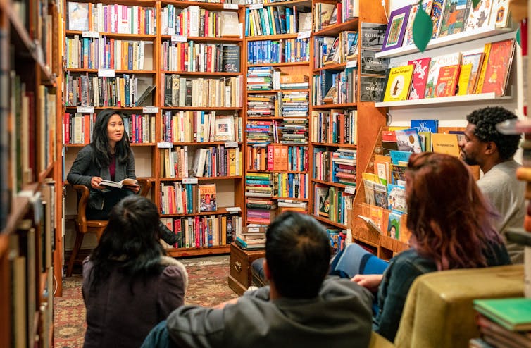 a woman reads from a book to a small audience in a bookstore