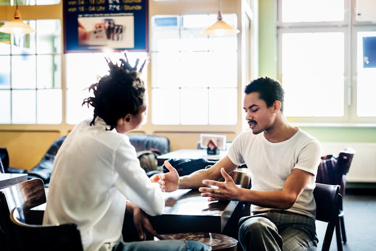 two young men in conversation, seated at a table