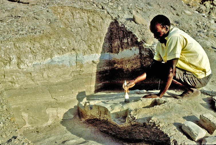 man squats on excavation surface, brushing with paintbrush