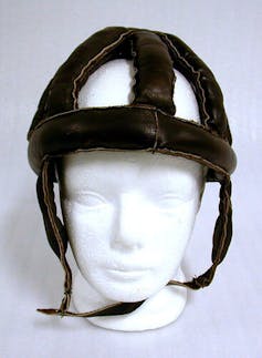 A bike helmet made from leather strips connected into a dome on the head of a mannequin.