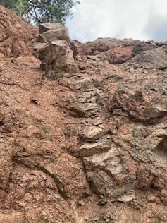 A cliff side showing a long strip of lighter color Tava cutting through Pikes Peak Granite. The injectite here is 5 meters tall