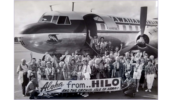 A group of people standing outside a plane holding a sign that says 'Aloha from Hilo'