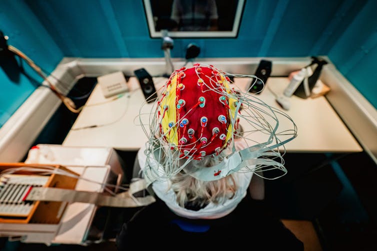 Person wearing an EEG cap, sitting at a desk in front of a computer