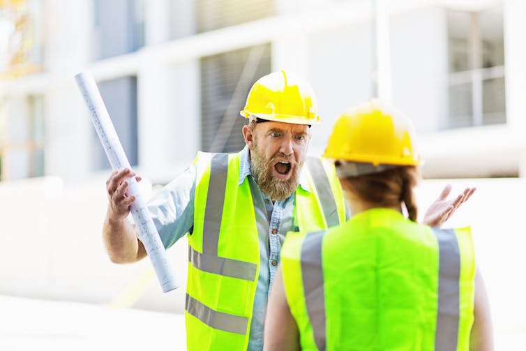 man yelling at woman, both in hard hats and high-visibility vests