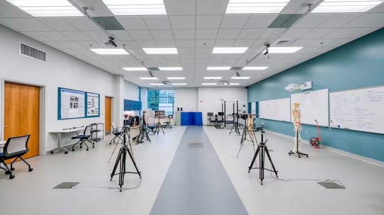 A large room with a gray strip down the center of the floor, with a square plate in the middle and cameras on tripods lining it.