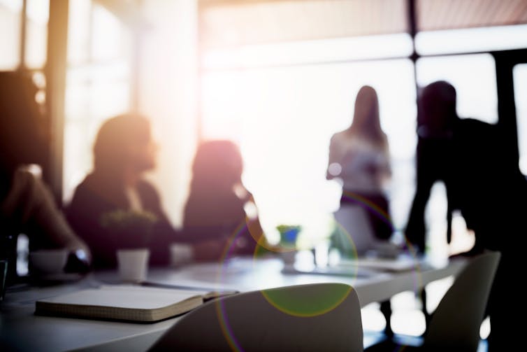 out of focus view of several people seated and standing around a conference table