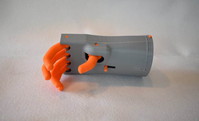 Mechanical hand with plastic orange fingers extending from a plastic gray palm and wrist