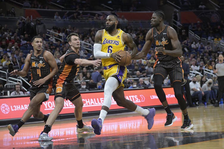 Four basketball players running around the court, the center one, Lebron James, holding the basketball.