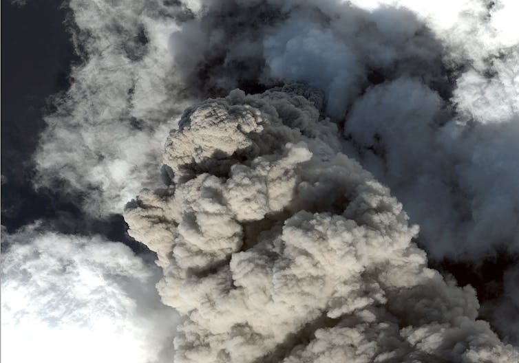 aerial view of an erupting volcano with billowing grey smoke and ash