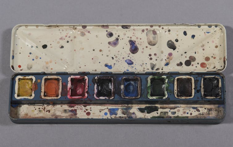 an open box of watercolor paints with splatters of color on the case