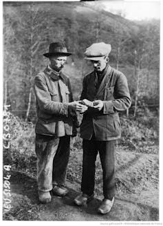 two men in jackets and caps hold and examine an object outdoors