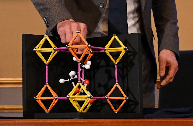 A model constructed out of metal bars and spheres, showing a cubic structure with smaller molecule models in the center.