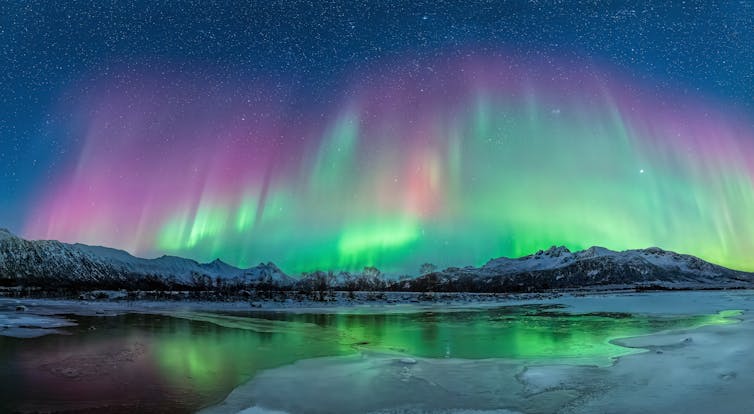 Bands of colorful light in the night sky above a snowy ridge.