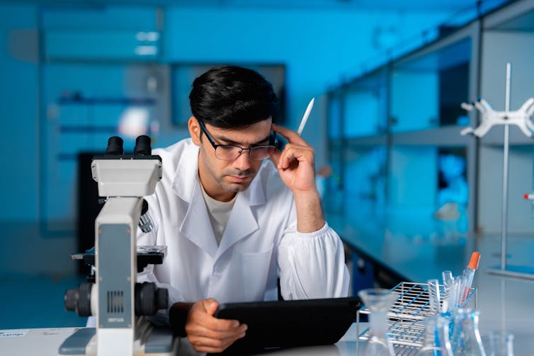 man in white coat in lab looking at tablet