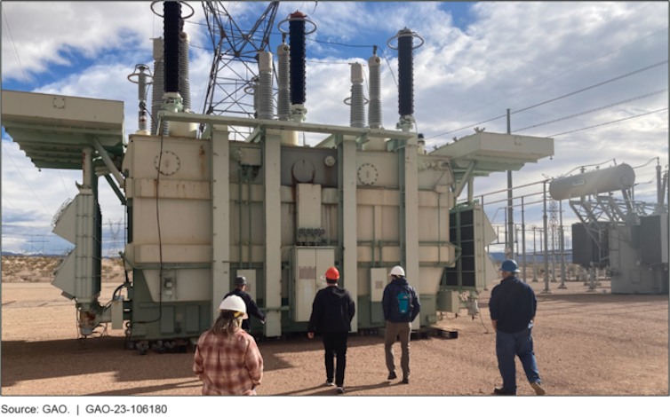 people wearing hardhats in front of electrical equipment the size of a small house